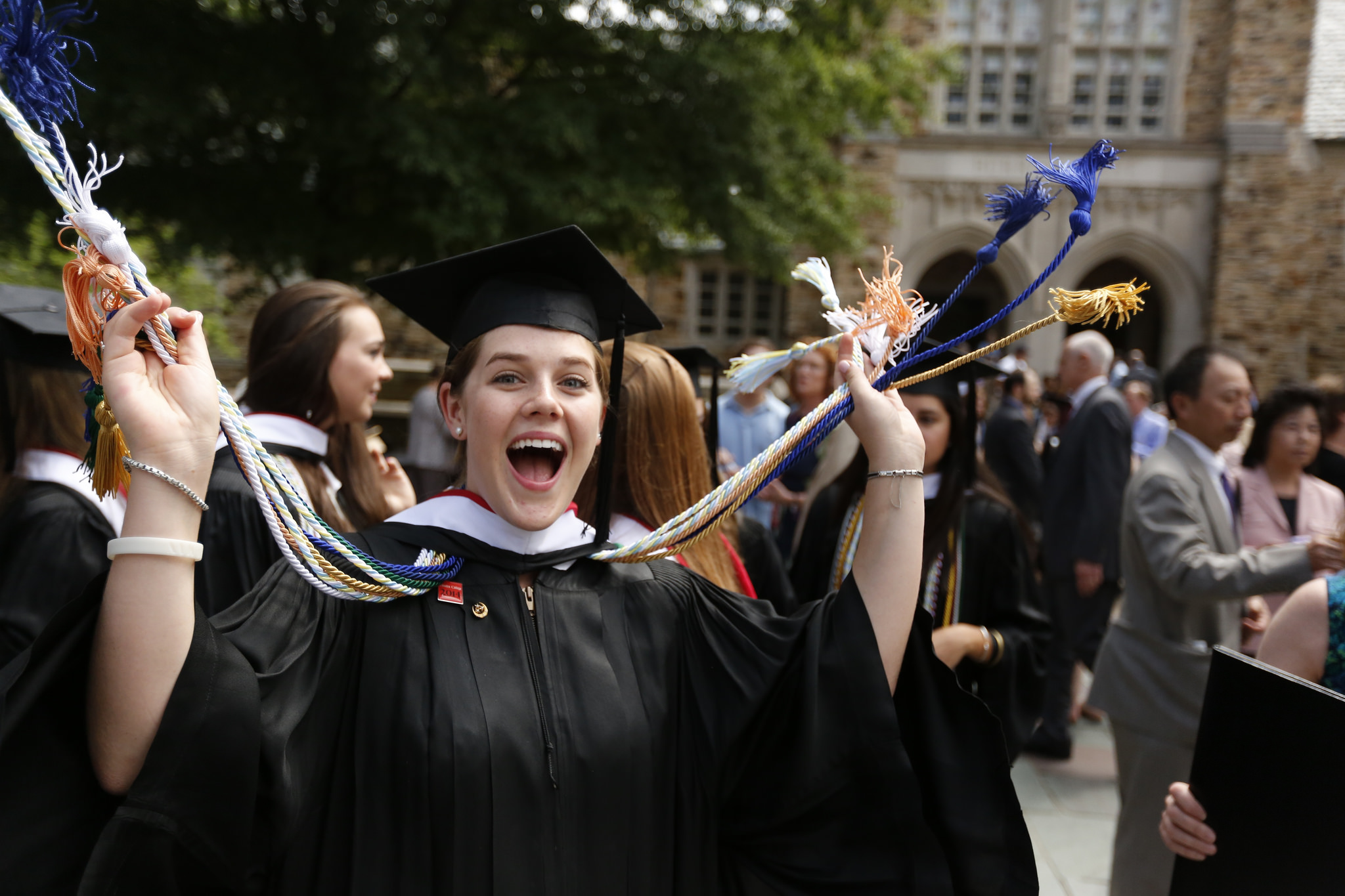 An excited student in graduation regalia smiles at the camera