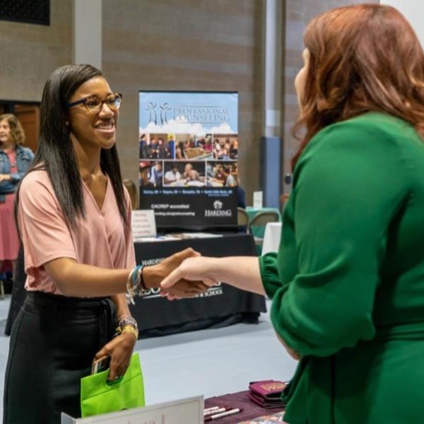 Two women shake hands at a recruiting fair.