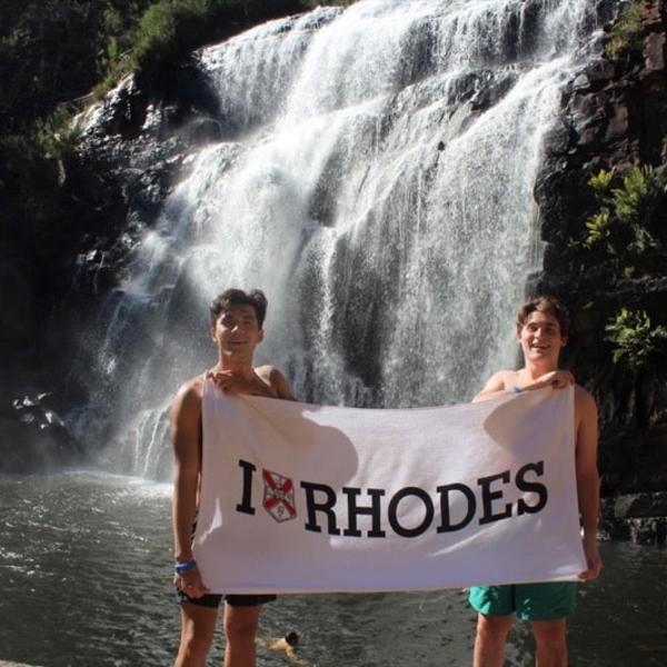 Two young men stand with an "I Heart 好色先生TV" banner in front of a rushing waterfall.