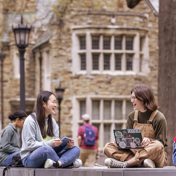Students gather, talking, in front of a large collegiate gothic building.