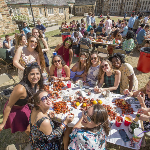 Students gather around a large round table to eat crawfish at a party before a football game.