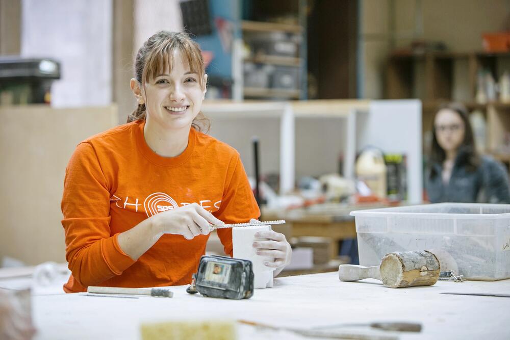 A young woman in an orange shirt files down the end of a mold.